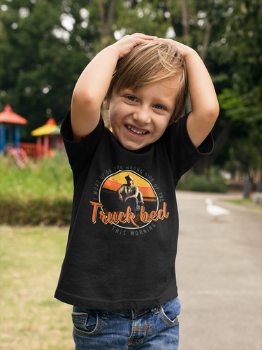 A young boy wearing a black t-shirt with a graphic design and text, smiling and posing in a park.
